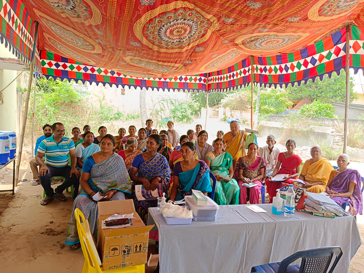 Women of the Prague Turmeric farm seated under a pavilion to be briefed about the medical fund being set up for them.