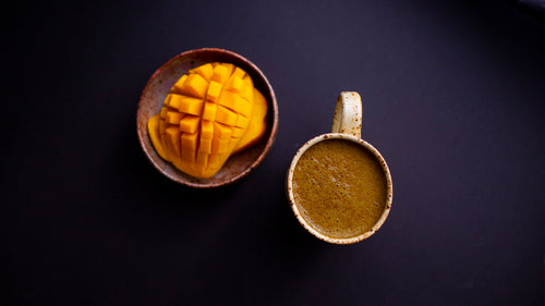 Ghee Coffee in a mug alongside a perfectly cubed half of a mango