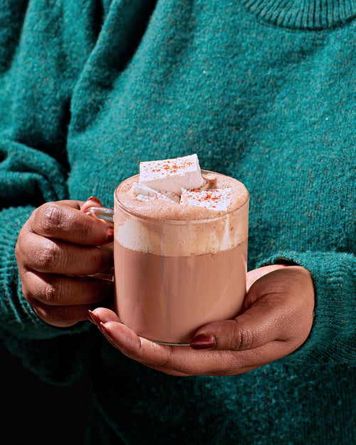 hot cocoa in a glass with milk foam and marshmallow on top