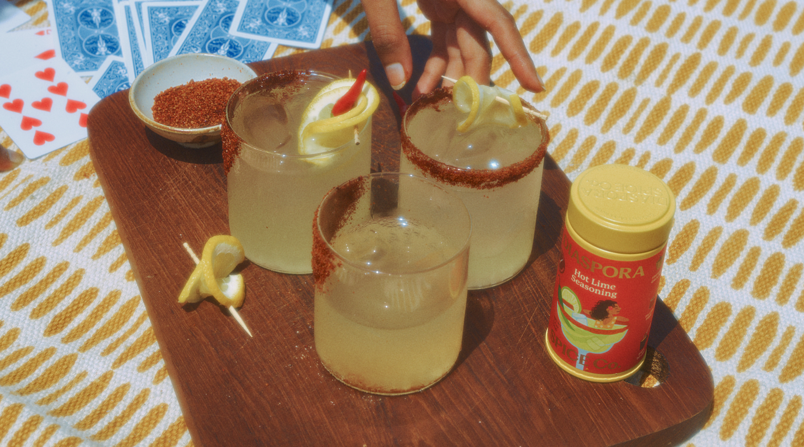 Hot Lim Seasoning tin kept on a picnic blanket along with 2 margarita glasses with a cocktail rim.